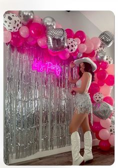 a woman standing in front of a wall with balloons and confetti on it