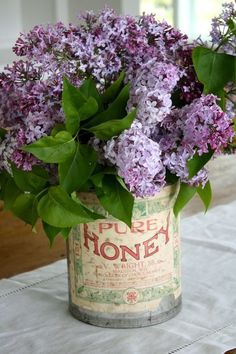 purple flowers in an old tin can on a white tablecloth with a window behind it