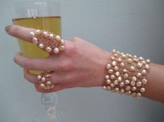 a woman's hand holding a wine glass with pearls on it and a gold bracelet