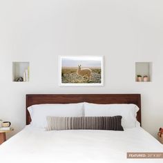 a bed with white sheets and pillows in a bedroom next to two pictures on the wall