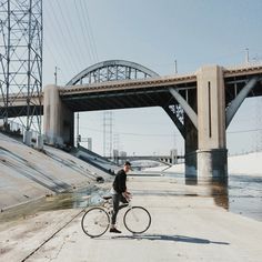 a man riding a bike down a street next to a bridge