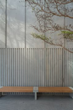 a wooden bench sitting in front of a metal wall with a tree on it's side