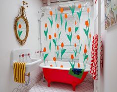 a bathroom with a red bathtub and orange flowers on the shower curtain next to it