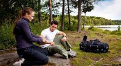 a man and woman sitting on the ground next to a body of water with trees in the background