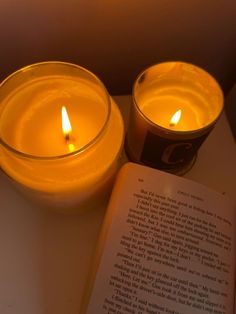 two lit candles sitting next to an open book