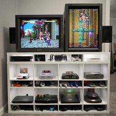 two televisions sitting on top of a white shelf filled with video game controllers and games