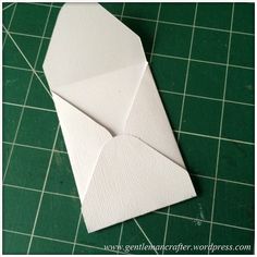 an origami envelope sitting on top of a green cutting mat with white paper