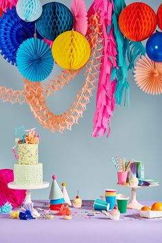 an assortment of colorful party decorations and paper fans hanging from the ceiling over a table