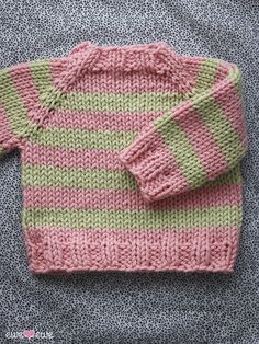 a pink and green sweater sitting on top of a bed