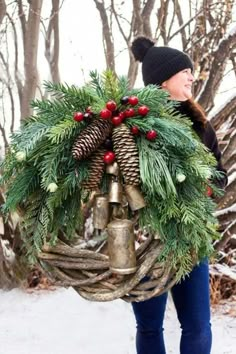 a woman carrying a wreath with bells and pine cones on her back in the snow