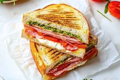 a cut in half sandwich sitting on top of a piece of paper next to tomatoes