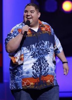 a man standing on top of a stage with a microphone in his hand and wearing a colorful shirt