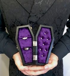 the man is holding two rings in his hands, one with purple velvet and the other with white diamonds