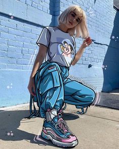 a woman with blonde hair sitting on the ground next to a blue wall and wearing sneakers