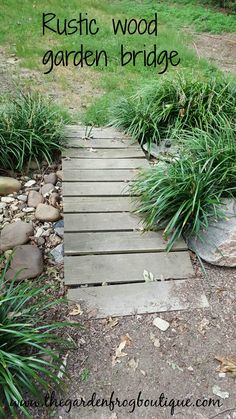 a wooden walkway surrounded by grass and rocks with the words rustic wood garden bridge above it