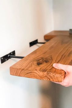 a hand is holding the edge of a wooden table with two black brackets on it