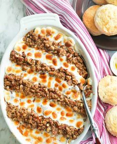 a casserole dish filled with meat and cheese on a striped towel next to muffins