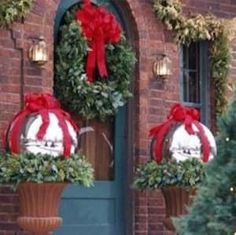 two christmas wreaths on top of planters in front of a door