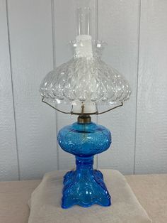 a blue glass table lamp sitting on top of a white cloth under a light fixture