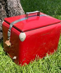 an old red box sitting in the grass next to a tree with a tag on it