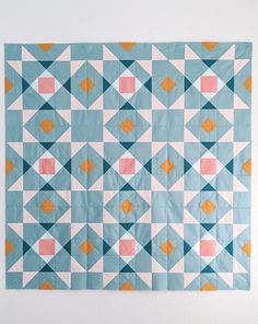 a blue and pink quilt hanging on the wall next to a white wall with an orange triangle