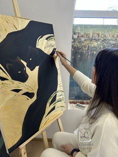 a woman is painting on an easel in front of a window