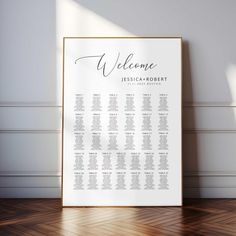 a white and gold wedding seating chart on a wooden floor in front of a wall