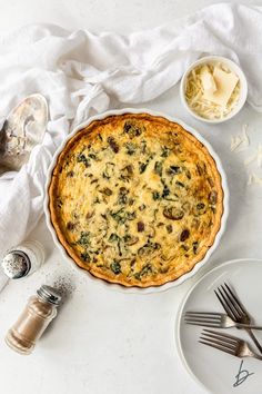 an overhead view of a quiche with cheese and spinach on the table next to utensils