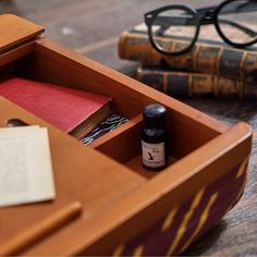 an open wooden box with some books and eyeglasses on the table next to it