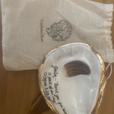 an open oyster shell with writing on it next to a white napkin and gold trimming