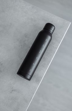 a black water bottle sitting on top of a cement floor next to a white wall