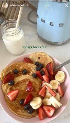 pancakes with strawberries and blueberries are on a plate next to a glass of milk