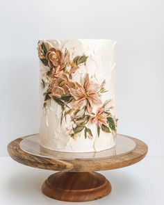 a white cake with flowers on it sitting on a wooden stand next to a wall