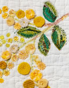 an embroidered piece with yellow flowers and green leaves on white fabric, surrounded by other things