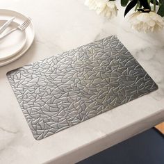 a place mat on top of a table next to a white plate and silver utensils