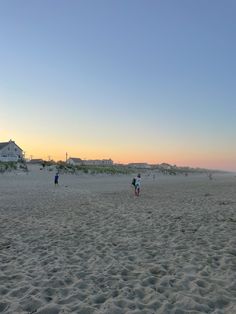 two people on the beach flying a kite in the distance with houses in the background