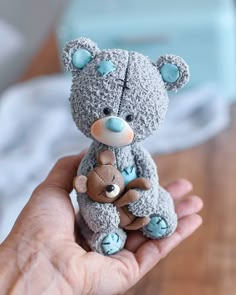 a hand holding a small gray teddy bear