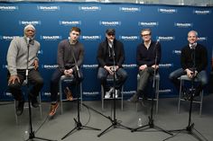 five men sitting on chairs in front of a blue wall with the words shamut