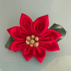 a large red flower with green leaves and gold balls on it's center piece