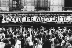 a large group of people standing in front of a building with a banner that reads women of the world unit