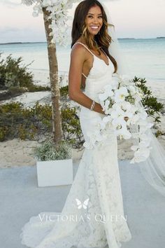 a woman in a wedding dress standing on the beach holding a bouquet of white flowers