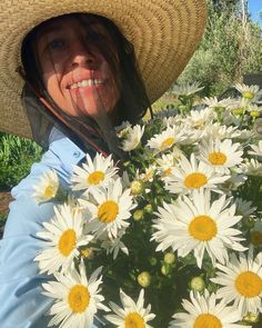 a woman wearing a straw hat and holding a bunch of daisies in her hands