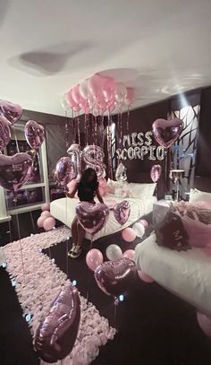 a woman sitting on a bed surrounded by pink and silver balloons in the shape of hearts