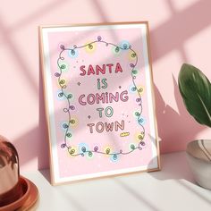 a pink poster with the words santa is coming to town next to a potted plant