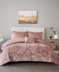 a bed with pink comforter and pillows in a room next to a painting on the wall