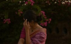 a woman in a pink sari is talking on her cell phone while standing outside