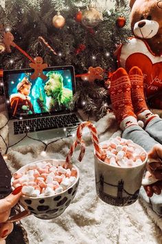 two people are eating marshmallows in front of a laptop and christmas tree