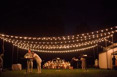 two men are standing in the grass with lights strung over them