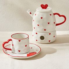 two cups and saucers with hearts painted on them sitting next to a teapot