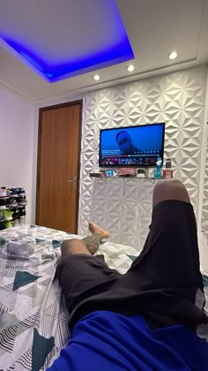 a person laying on top of a bed in front of a flat screen tv mounted to the wall